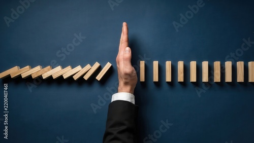 Businessman stops falling dominoes with his hand, preventing a chain reaction. Risk management concept.
