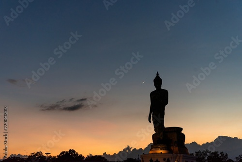 Foto Silhouette Stand big Buddha Statue during sunset Light background at park of Thailand temple Yellow orange silhouette dark shadow of image Buddha statue stand Buddha tall walk in sunlight clouds