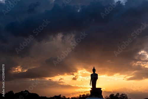 Bild auf Leinwand Silhouette Stand big Buddha Statue during sunset Light background at park of Thailand temple Yellow orange silhouette dark shadow of image Buddha statue stand Buddha tall walk in sun light cloud