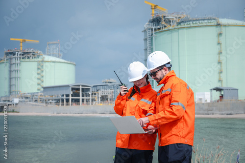 Male and female petroleum engineers discussing work while inspecting the construction of oil pipelines at a petroleum refinery.