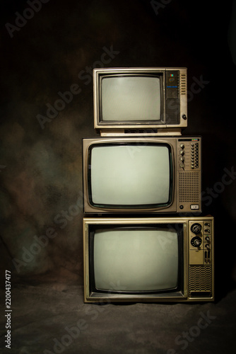 Three retro old televisions pile with blank screen on a dark background