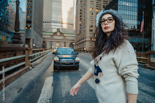 Woman walking on street in New York City. Female pedestrian crosses road near Grand Central Terminal with car in background.