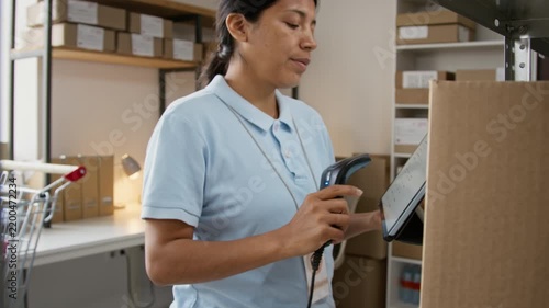 Hispanic young woman warehouse worker tapping digital tablet while holding barcode scanner. Clip suitable for supply chain logistics, inventory management, and e-commerce distribution