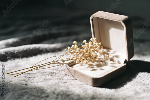 Open cream velvet lined jewelry box with a gold earring and dried flowers on a white blanket