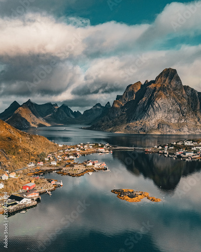 Vertical aerial view of Reine village with Olstind mountain reflection in fjord under dramatic sky in Lofoten Norway