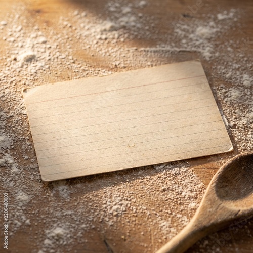 Blank lined recipe card on floured wooden table with spoon