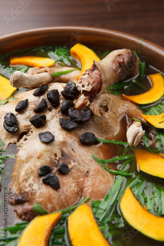 Bild auf Leinwand Korean whole duck soup with black garlic and pumpkin slices in earthen bowl