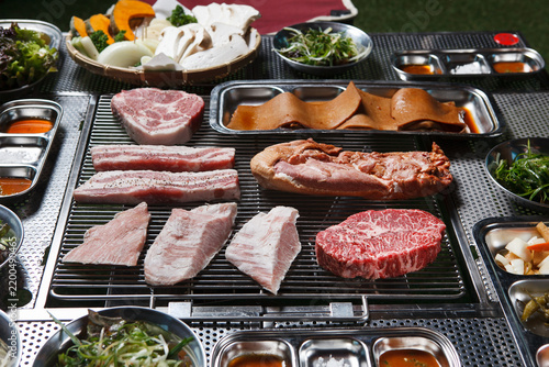 Assorted raw pork and beef cuts on barbecue grill with vegetables and sauces