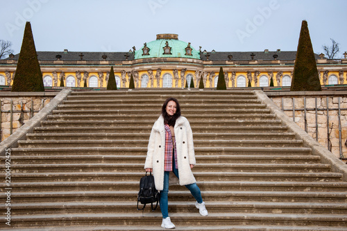 Stylish woman in autumn coat at palace stairs. Woman stand at stairs to palace. Girl casual style outdoor. Touristic and travel destination. Girl tourist walking stairs. Sightseeing and landmark