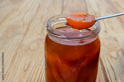 Homemade Apricot Jam in Glass Jar with Spoon on Wooden Background