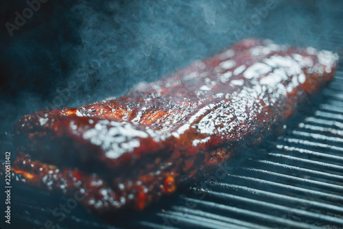 Barbecue pork ribs smothered in homemade bbq sauce smoking on a pellet grill smoker for dinner. 