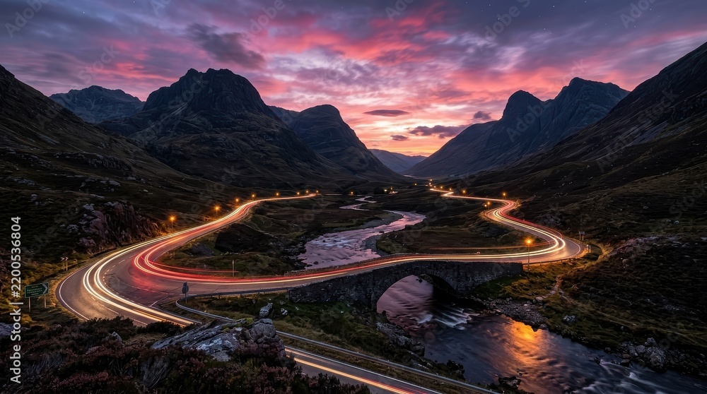 Obraz premium Dramatic Sunset over Glencoe Valley with Car Light Trails on a Winding Mountain Road and Stone Bridge in Scotland