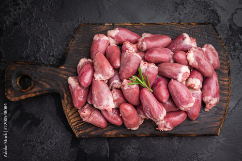 Fotografie Raw chicken hearts with rosemary on dark wooden board and black stone background, fresh poultry offal ready for cooking