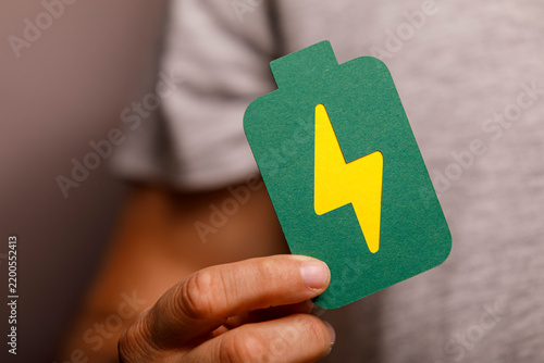 A person holds a paper cutout of a green battery with a yellow lightning bolt, symbolizing energy.