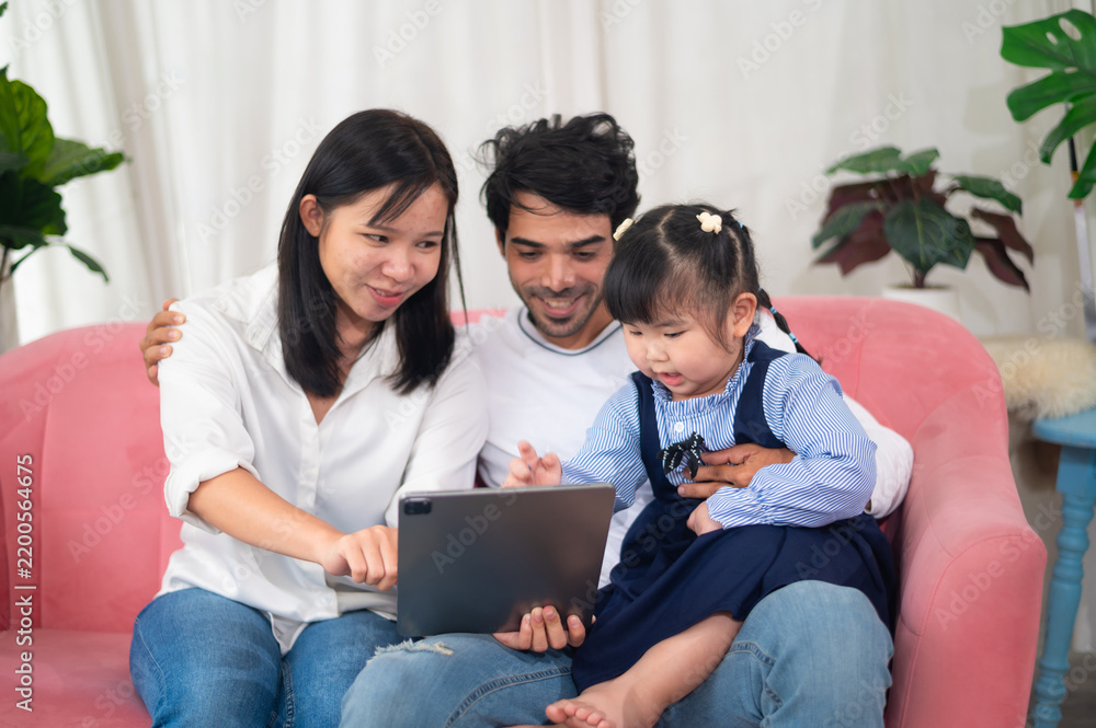 Fototapeta premium A loving family enjoys quality time together on a cozy sofa, sharing laughter and learning while watching a tablet, highlighting family bonds and joy.