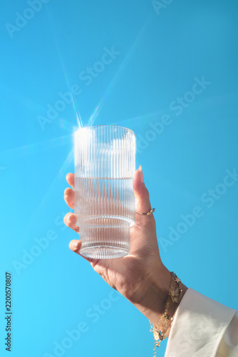 Hand holding a glass of water against a clear blue sky