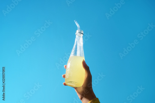 A refreshing glass bottle of lemonade is held up against a bright sky