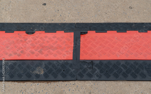 Картината върху платно Heavy-duty red and black modular cable protector ramp with checker plate anti-slip texture on a concrete surface, providing temporary safety for wires and hoses in industrial or event settings