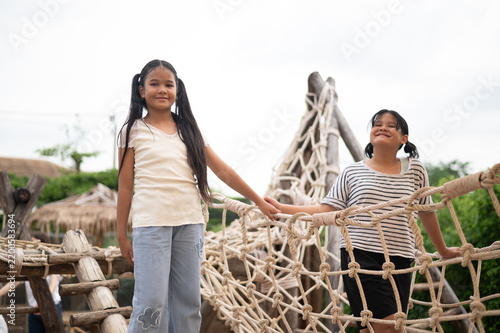 Принти на полотні Two girls enjoying fun playtime on a rope bridge, showcasing friendship and joy in a playful outdoor setting, perfect for children's themes