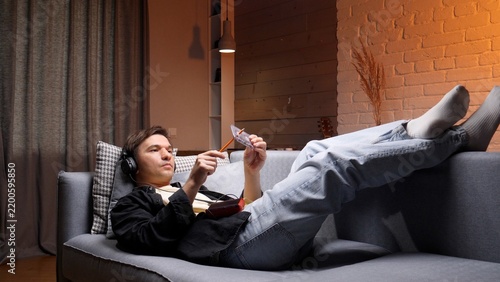 Man relaxing on sofa at home, wearing headphones and rewinding a vintage cassette with a pencil while enjoying nostalgic music in a cozy, laid back evening setting