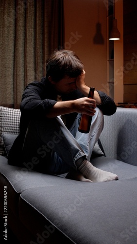 Obraz na płótnie Man experiencing sadness, holding a bottle of an alcoholic beverage while sittin