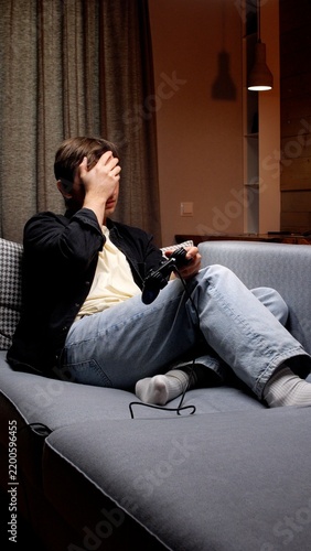 Obraz na plátně Young man sitting on a sofa with a controller, covering his face in disappointme