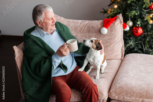 Foto Smiling senior man holds mug beside small dog on sofa