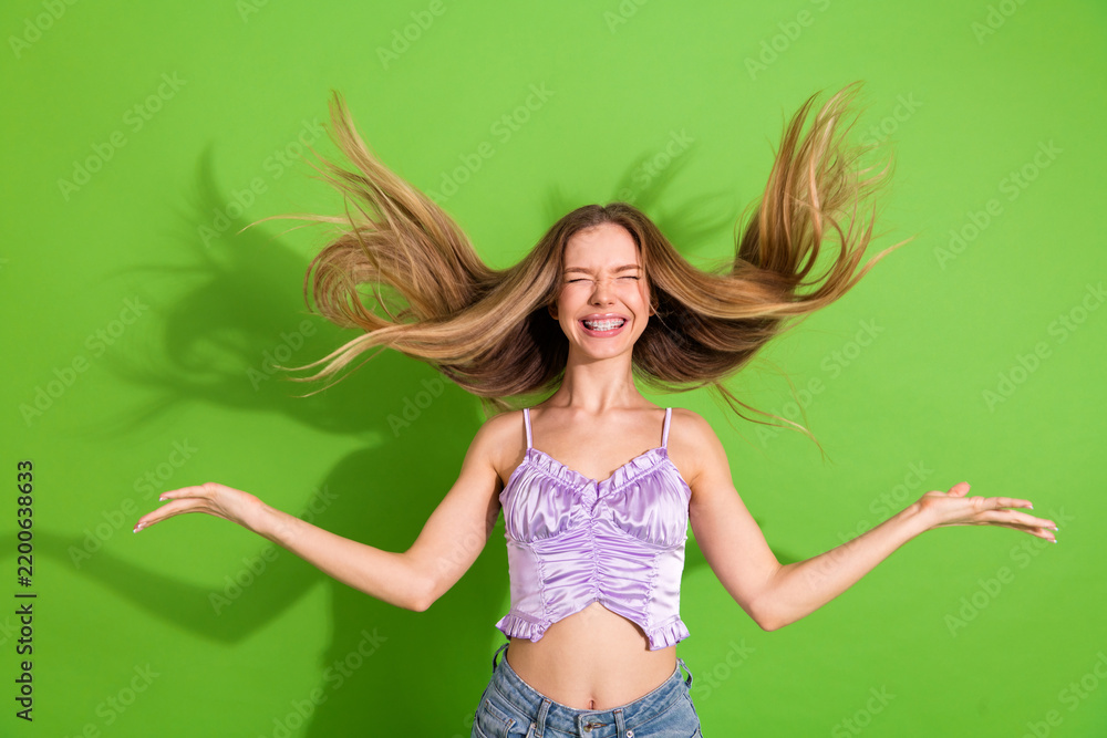 Fototapeta premium Glamorous young woman with long blonde hair jumping with joy against a vivid green background in a casual stylish lifestyle shot for fashion advertising