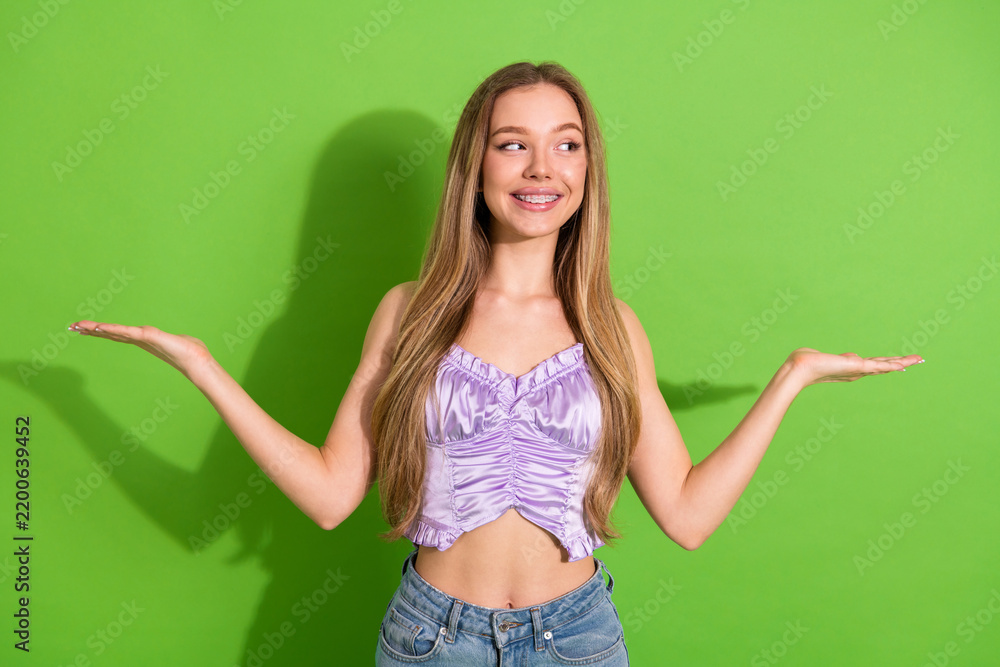 Obraz premium Young glamorous woman long blonde hair wears lilac top and smiles arms outstretched green background for fashion lifestyle advertising and shopping appeal