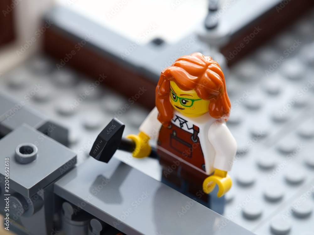 Obraz premium Tambov, Russian Federation - June 24, 2026 A close-up shot of a Lego minifigure woman with red hair holding a hammer while working on a grey structure