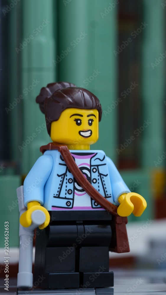 Fototapeta premium Tambov, Russian Federation - June 24, 2026 A close-up shot of a Lego woman minifigure with a crutch and a shoulder bag standing on a city street.