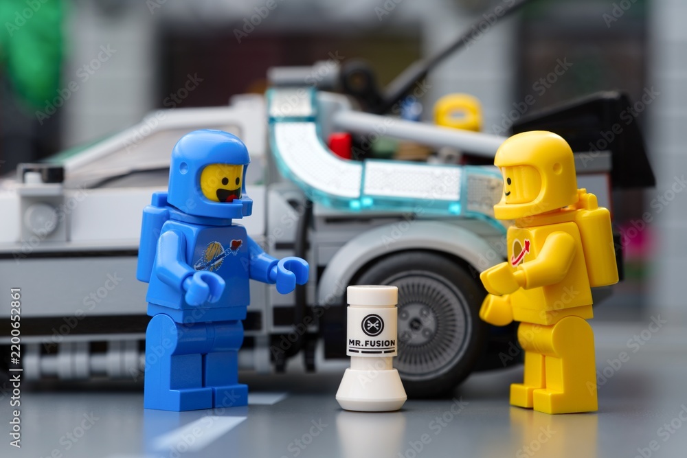 Obraz premium Tambov, Russian Federation - September 17, 2026 Blue and yellow Lego spaceman minifigures standing next to a Mr. Fusion generator with a DeLorean time machine in the background.