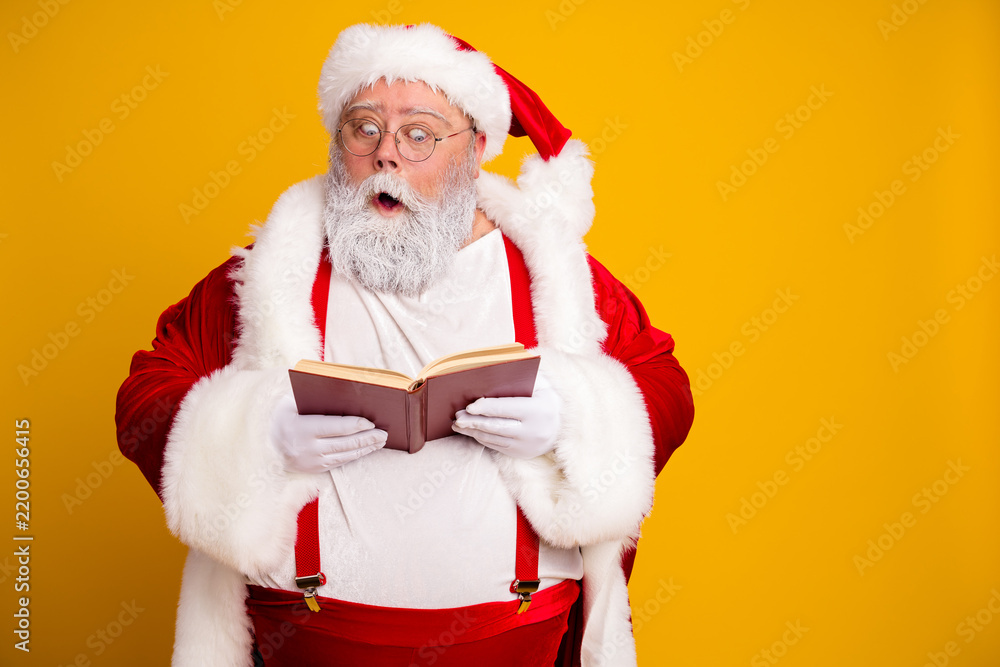 Obraz premium Santa Claus reading a book with a surprised expression against a bright yellow background, festive holiday portrait in classic red suit and white beard