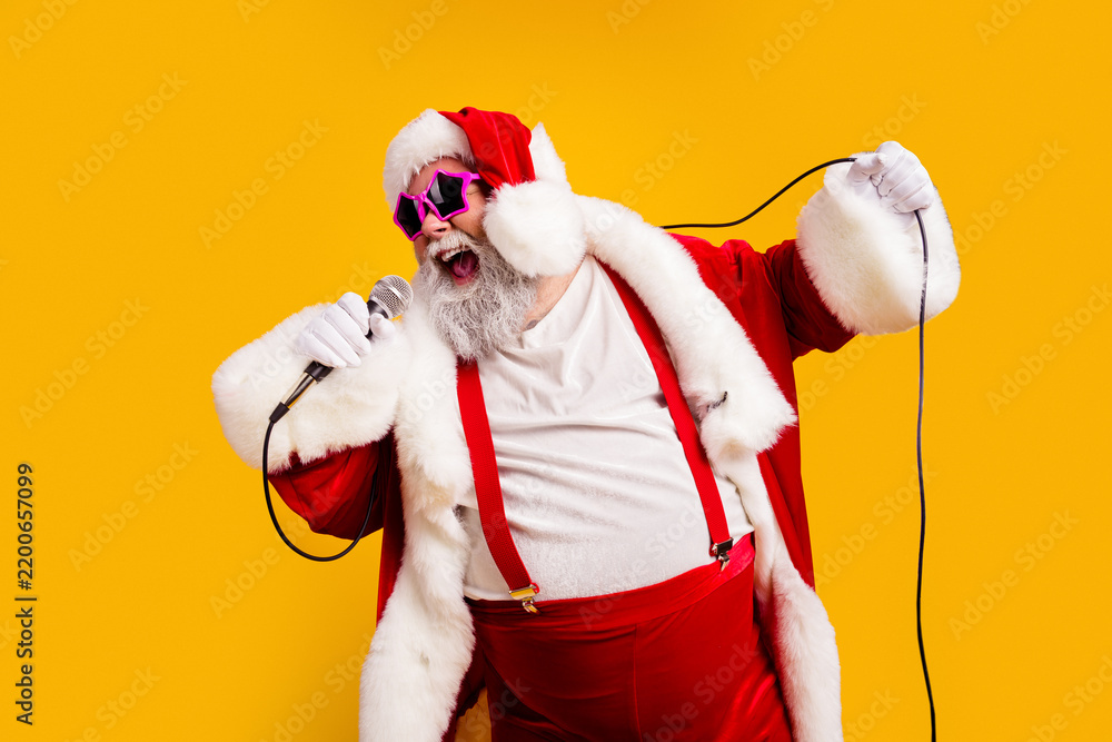 Obraz premium Santa Claus singing into a microphone with pink sunglasses and festive costume on a bright yellow background