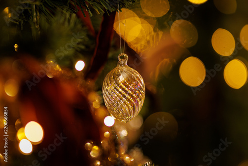 Glass Christmas ornament hanging on pine tree with golden lights close up