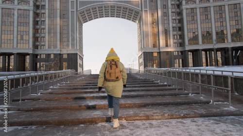 Woman tourist climbs street staircase against background of arched passage in building while exploring Astana in winter