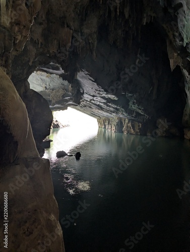 Konstfotografi Looking from the cavern darkness toward a brightly lit cave exit over calm subterranean waters reflecting daylight