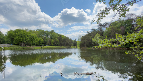 Obraz na plátně Wooded pond with a wooden footbridge on the left, mirror-like reflections of clo