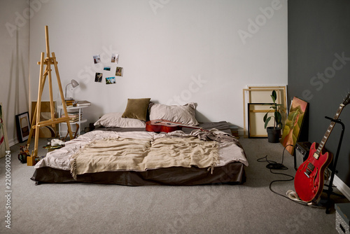 Creative bedroom studio featuring musical instruments, easel, and mattress on floor. Scene depicting artistic youth lifestyle, ideal for music or art advertising