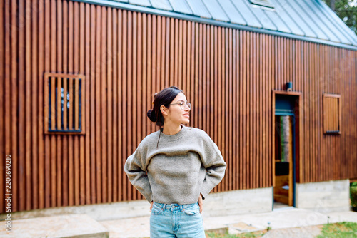 Фотография Woman smiling, standing outdoors in front of a modern wooden cabin, enjoying a p