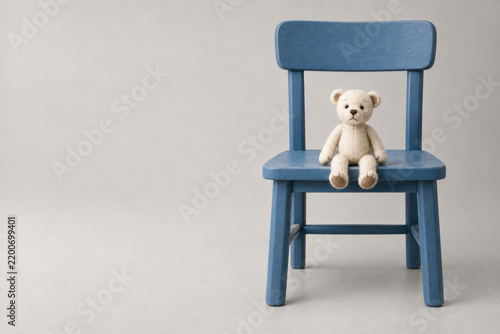 Small teddy bear sits on a blue wooden chair. Space for text.