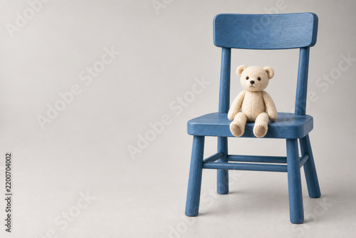 Small teddy bear sits on a blue wooden chair. Space for text.