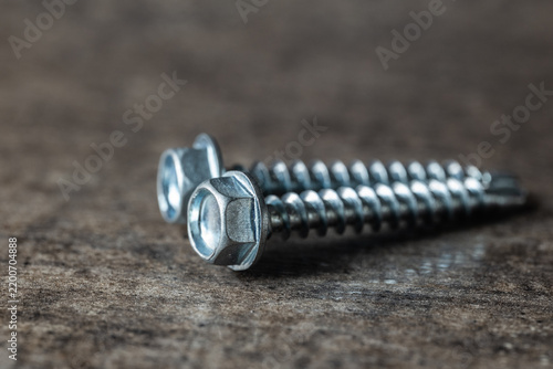 Two metal self-tapping screws with hexagonal heads lying on a textured gray concrete surface, close up