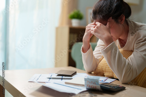 Fotografie Stress woman sitting with bills, calculator, cash and financial documents at hom