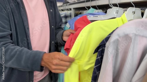 Close-up of a man browsing secondhand dress shirts on a clothing rack while shopping for affordable menswear at a thrift store. 15418  