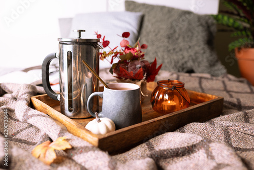 Hygge style composition with candle, cup of tea, autumn decorations and books on warm blanket. Cozy home interior. Autumn mood concept.
