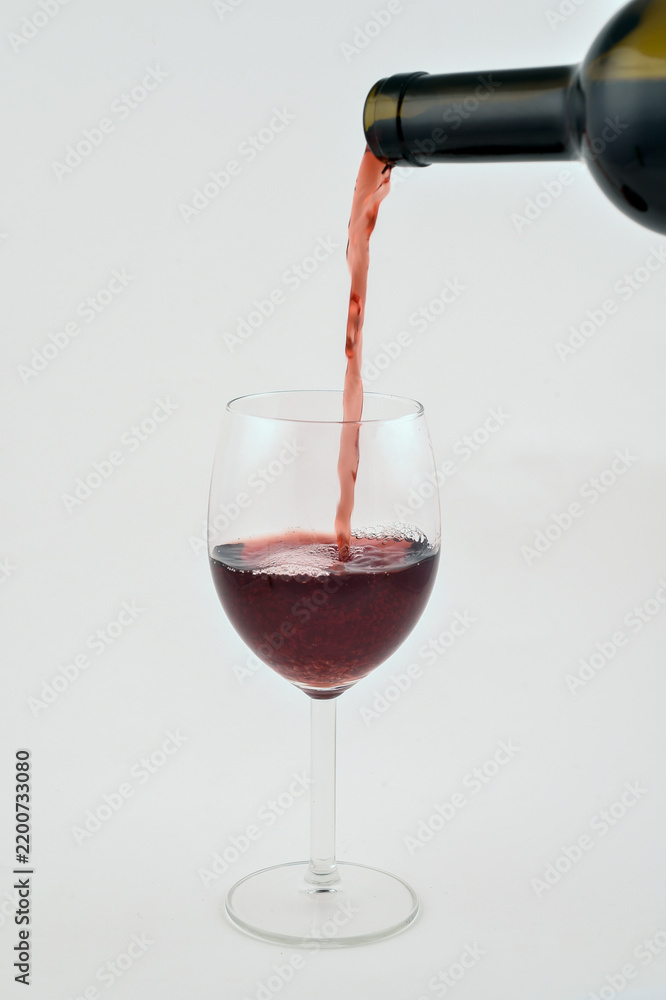 Obraz premium Red wine pouring from a dark bottle into an elegant clear glass on an isolated bright white background, symbolizing celebration, tasting, luxury, and fine dining.