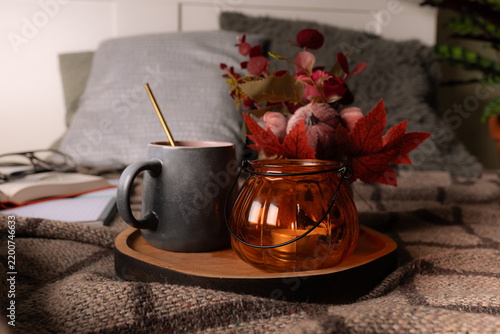 Hygge style composition with candle, cup of tea, autumn decorations and books on warm blanket. Cozy home interior. Autumn mood concept.