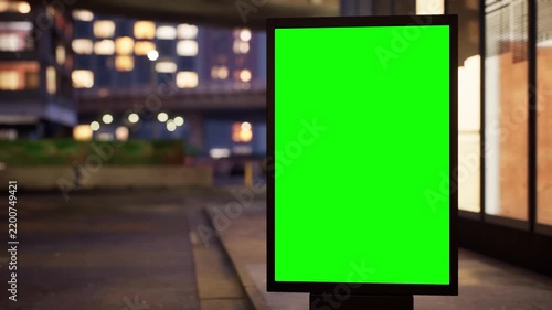 Vertical green screen citylight sign on a downtown sidewalk at dusk as the city lights come on, clear sky. Time lapse of city traffic, bokeh lights and moving cars. Clean chroma key area for