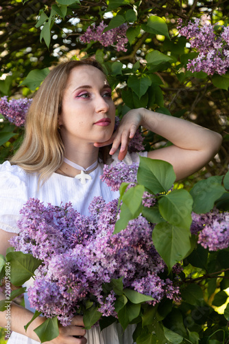 Romantic outdoor portrait with blooming lilacs and feminine spring style